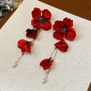 Elegant red fabric flower tassel earrings with pearls displayed on a beige textured board