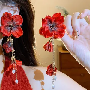 Detailed close-up of elegant red fabric flower earrings with long gold tassels and white pearls