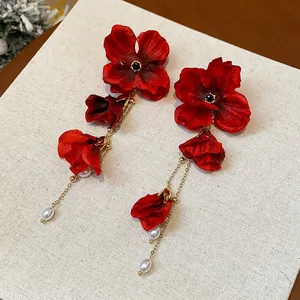 Detailed macro view of red fabric flower earrings with gold tassels and pearls