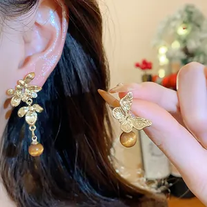 Detail shot of asymmetrical golden butterfly and flower earrings with brown beads