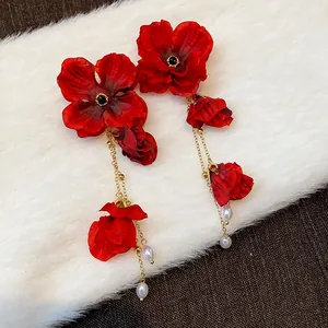 Detailed view of handmade red fabric flower earrings with gold chain tassels and pearls.