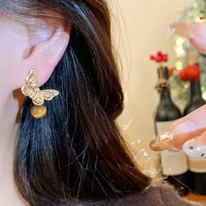 Close-up of a vintage golden butterfly stud earring with a brown pearl drop worn on the ear