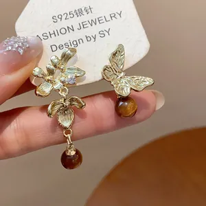 Detailed macro view of asymmetric gold flower and butterfly earrings with brown beads