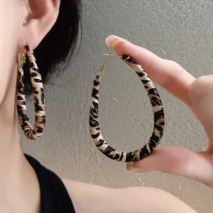 Vista macro de pendientes de aro envueltos en cuero con estampado de leopardo y detalle.