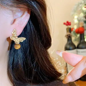 Close-up of golden butterfly earring with brown stone bead worn on ear detail view
