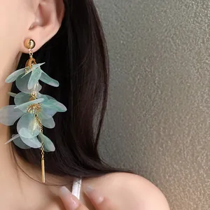 Gros plan d'un mannequin portant des boucles d'oreilles fleurs vertes et glands dorés