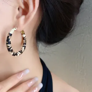 Primer plano de elegantes pendientes de aro con estampado de leopardo usados por modelo.