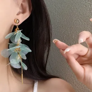 Détail de boucles d'oreilles pendantes à fleurs en tissu vert et aiguille en argent.