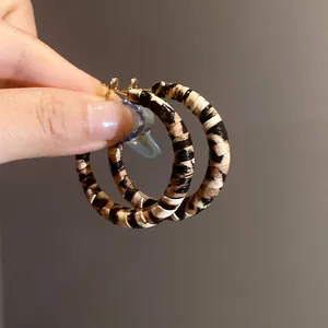 Primer plano de elegantes pendientes de aro envueltos en cuero de leopardo con plata