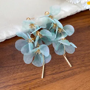 Gros plan de boucles d'oreilles fleurs en tissu bleu clair avec glands dorés délicats