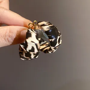 Detalle de pendientes de aro envueltos en cuero con estampado de leopardo dorado.
