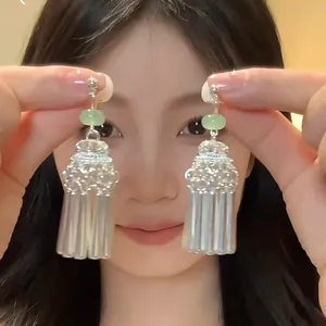 Close-up of ethnic style silver tassel earrings with green beads held by a female model