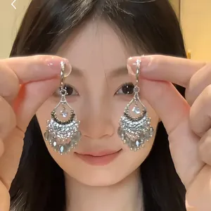 Close-up detail of ethnic water-drop tassel earrings with crystal fringe held by model