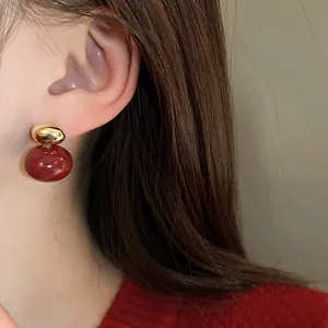 Macro detail of a vintage red bead earring with a golden stud worn on an earlobe