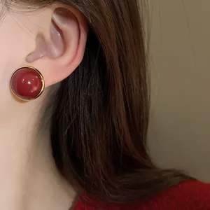 Detailed close-up of an elegant red round stud earring with a gold rim worn on the ear