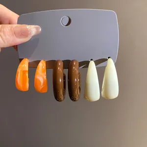 Detailed view showing a set of retro C-shaped acrylic earrings in marbled orange, brown and cream