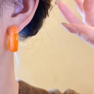 Close-up view of a marbled orange acrylic C-shaped hoop earring on a model's ear