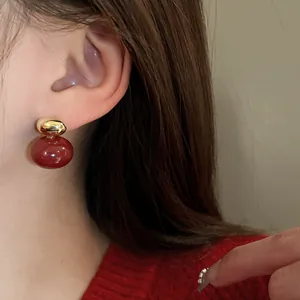 Detail showing a vintage-style red and gold ball stud earring worn on a model ear