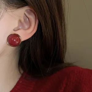 Close-up of a vintage red round stud earring with a gold border worn on a person ear.
