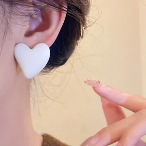 Close-up of a retro matte white heart-shaped acrylic stud earring worn on an ear.