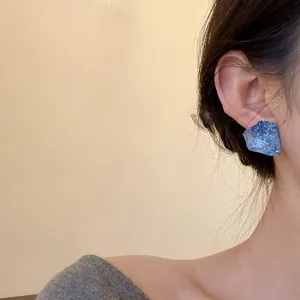 Detailed side view showing a stylish blue irregular resin stud earring worn by a model