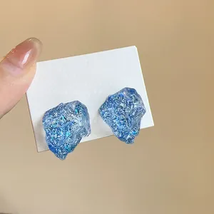 Close-up of irregular blue resin stud earrings with a shimmering glitter stone texture
