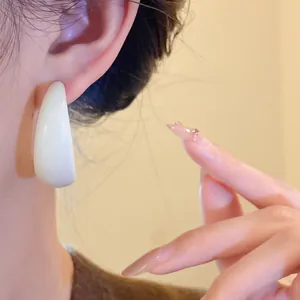 Close-up view of a vintage white acrylic C-shaped hoop earring worn on a model's ear.