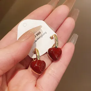 Close-up of glossy red heart earrings with gold-toned hooks on a display card.