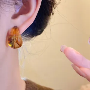 Macro view of vintage amber marbled acrylic teardrop earring worn by model on ear