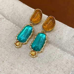 Close-up of premium irregular resin oval earrings featuring teal and amber color block design.