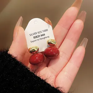 Close-up of red and gold drop earrings held on a hand, highlighting the glossy finish.