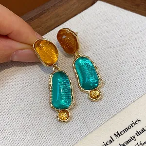 Detail view of irregular teal and amber resin earrings with textured gold-tone metal frame.