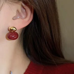 Close-up detail showing an elegant dark red and gold stud earring on a model's ear