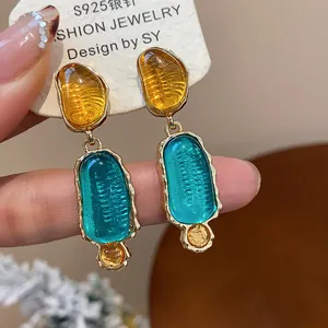 Detail view of luxury irregular resin drop earrings with turquoise and amber accents.