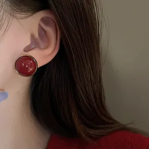 Elegant vintage red round stud earrings with gold border shown on a model's ear