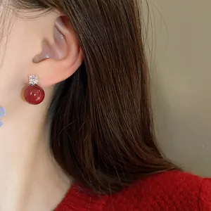 Detailed close-up view of elegant red pearl earrings with zircon stones on model's ear