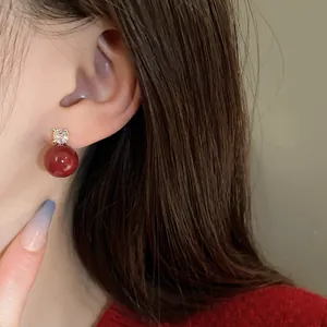 Close-up view of a vintage red pearl earring with a sparkling zircon stud worn on an ear.