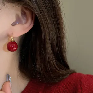Close-up detail of retro red pearl ball earring worn on ear with red sweater background.