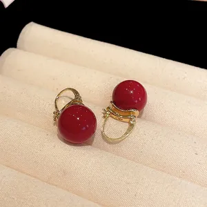 Close-up of vintage red pearl earrings with elegant gold-toned hooks on beige fabric