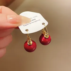 Close-up of elegant red pearl drop earrings with gold hooks on a white display card.