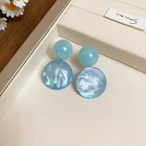 Macro view of blue pearlescent resin drop earrings displayed on a cream jewelry tray