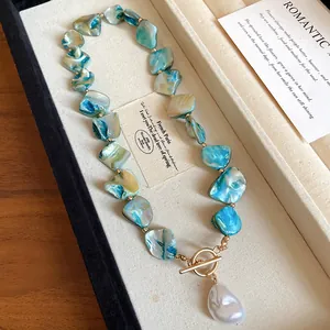 Detalle de collar de cuentas de concha azul con perla barroca y cierre OT en color dorado