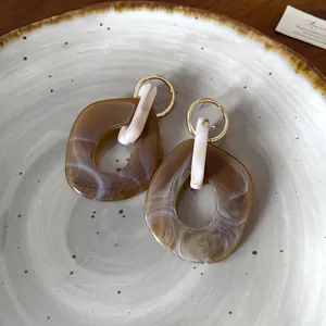 Macro dettagliata di orecchini a goccia in resina marmorizzata marrone con cerchi dorati