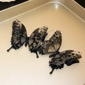 Detailed view of black 3D butterfly earrings with realistic wing patterns on a gold tray