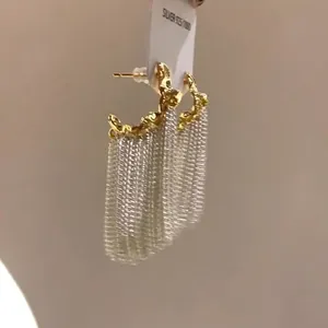 Dettaglio ravvicinato di orecchini a forma di C con lunghe nappe a catena d'argento.