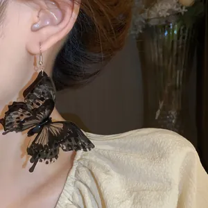 Close-up of oversized black 3D butterfly earrings with layered translucent wings.