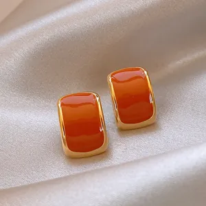 Detalle macro de pendientes de botón cuadrados en esmalte naranja y bordes oro