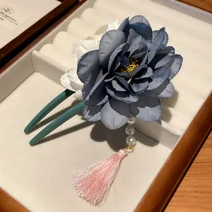 Nahaufnahme einer Haarnadel mit blauer Stoffblume, Perlen und einer rosa Quaste.