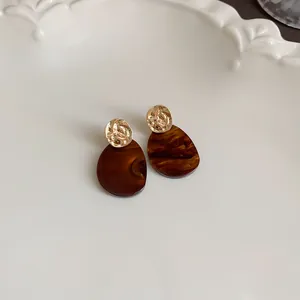 Detail of vintage Maillard brown tortoiseshell drop earrings with gold textured studs.