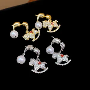 Close-up of rocking horse earrings with pearls and zircon detailing in gold and silver.